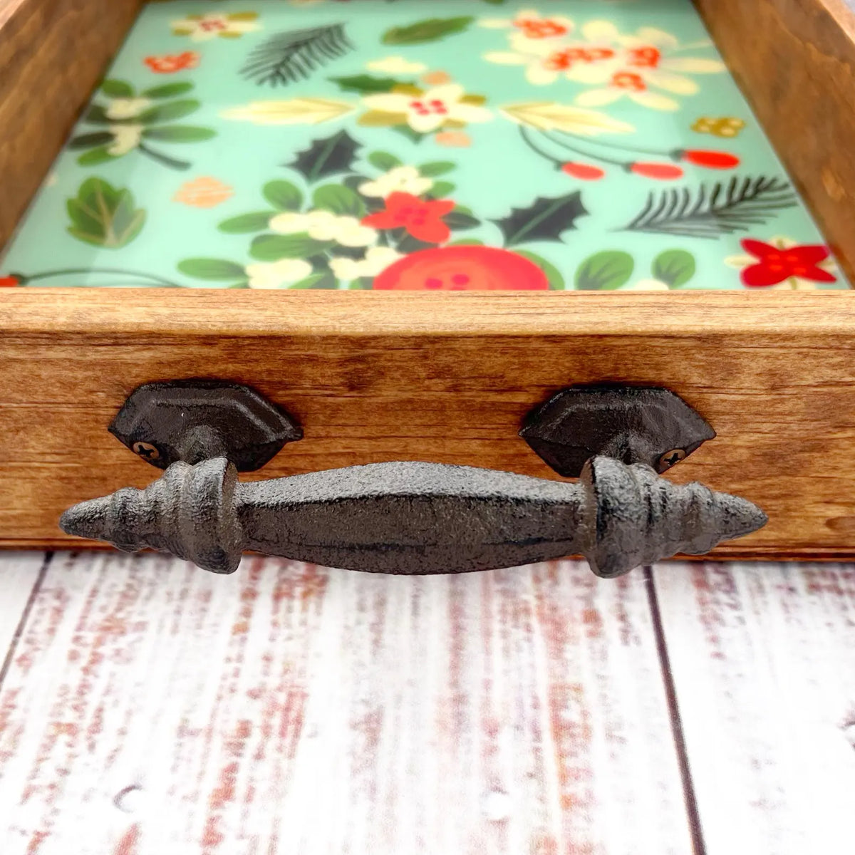Wooden tray with floral-patterned lining and decorative metal handle on a wooden surface.